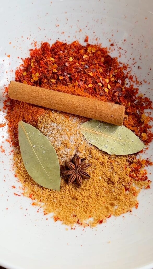 In a large bowl, combine the chili flakes, chili powder, cinnamon stick, anise, bay leaves, brown sugar, and salt.