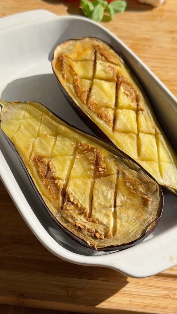 Cut the eggplant in half lengthwise. Using a sharp knife, score the flesh in a crosshatch pattern, being careful not to cut through the skin. Sprinkle with salt and drizzle with 2 tbsp olive oil. Place the eggplant halves cut side up on a baking sheet and bake for 20 minutes until softened.