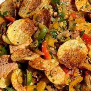 Golden, crispy baked potato slices being added to the salad, ready to be gently folded into the dressed vegetables and herbs.