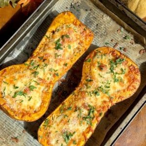 Golden roasted stuffed butternut squash halves on a baking tray, filled with creamy mushroom and spinach mixture and topped with melted cheese and parsley.