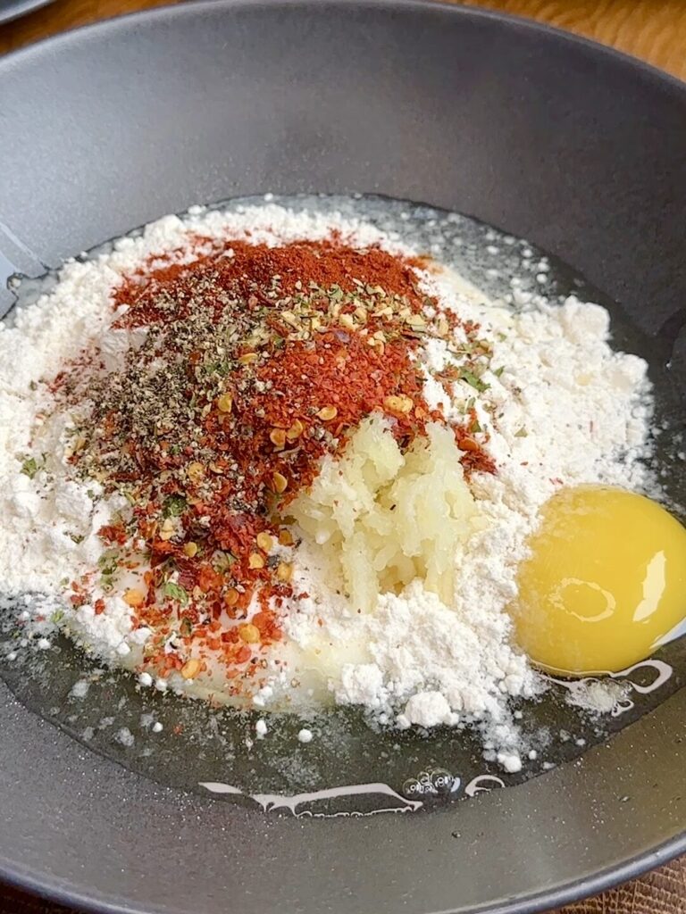 A mixing bowl with Greek yoghurt, egg, flour, garlic, and spices being whisked together to make a creamy coating for Cornflake Crusted Chicken Schnitzel