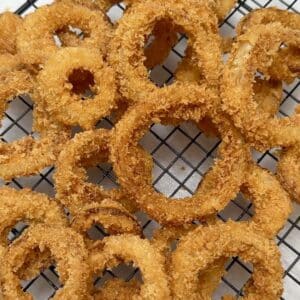 Freshly fried onion rings resting on a wire rack, golden and crispy as they cool.